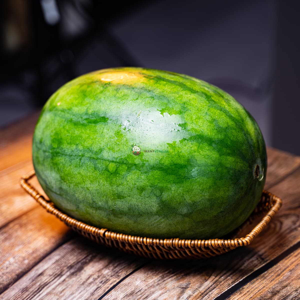 Watermelon on basket, on wood surface. Large fruit with green rind, red flesh, and black seeds.