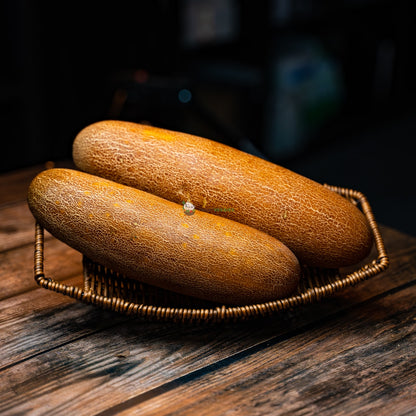 Two old, wrinkled cucumbers are laid on a wooden basket. The cucumbers are long and thin, with cracked and brown skin. They are both slightly curved