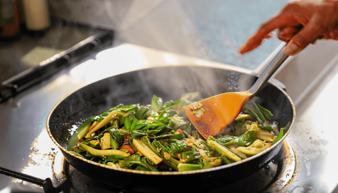 A close-up of a pan of sizzling sawi vegetable on a hot stove, the vibrant green leaves and stems glistening with oil and spices