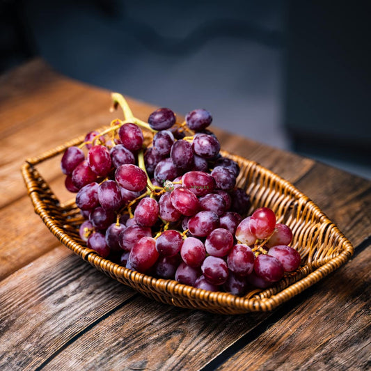 Purple seedless grapes in basket on wood surface - juicy, plump, and ready to eat. A healthy snack.