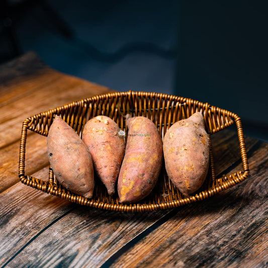 Four orange sweet potatoes in a basket on wood surface. Vibrant and fresh root vegetables with smooth skin and rough texture.