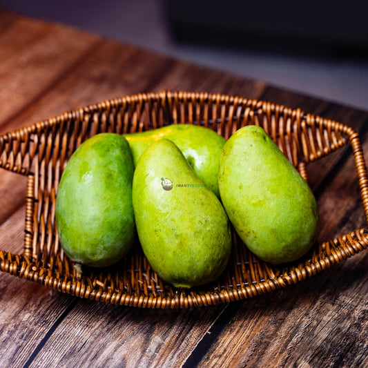 Four fresh green mangoes on wood surface - firm, shiny, without intact stems and small brown spots. A popular tropical fruit.