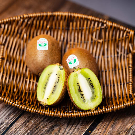 Three Zespri Green Kiwifruit, one halved, on a wooden basket. Fresh and vibrant, with green flesh and black seeds