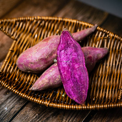 Four purple sweet potatoes, one cut half open, on a basket on wooden surface. Nutritious and colorful root vegetable
