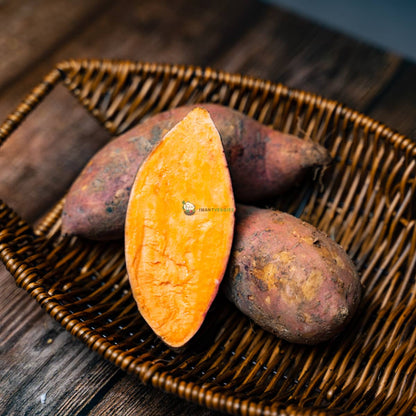 Four orange sweet potatoes, one cut open, on a basket over wooden surface. Fresh, healthy and nutritious tubers