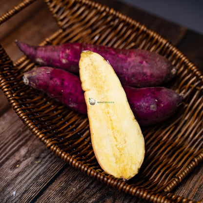 two full Japanese sweet potatoes, one halved, on a basket over wood. Purple skin, yellow flesh, and a tasty treat