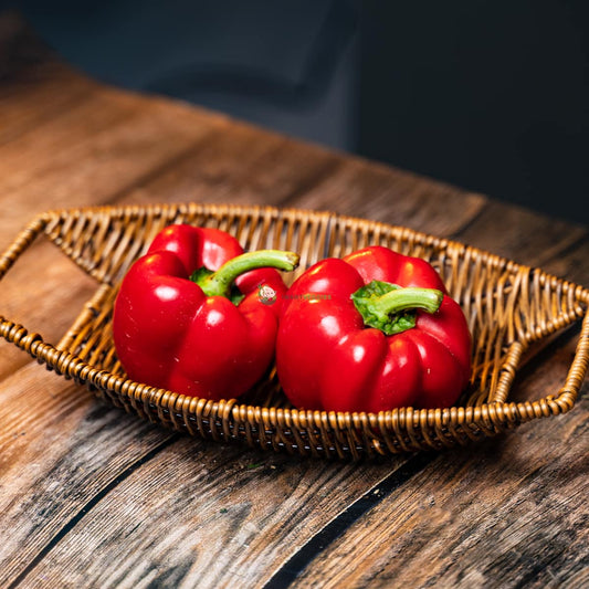 Two red bell peppers on a basket and wooden surface. Fresh and vibrant. A colorful addition to any dish