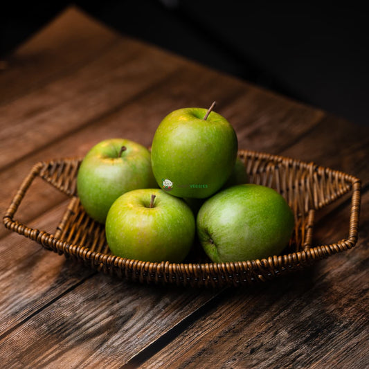 Four green apples in a basket on a wooden surface, one partially hidden by the others. Fresh, shiny.