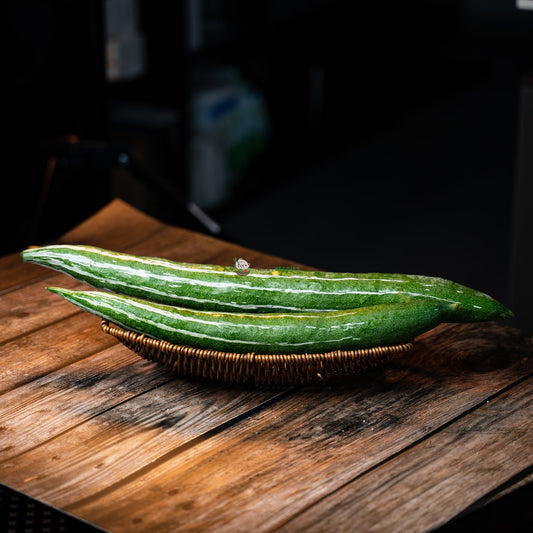 Two snake gourds on a wooden basket. Long, slender, green gourds with a smooth skin.