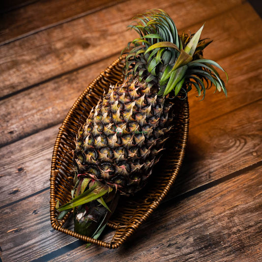 Ripe pineapple in basket on wooden surface. Prickly green leaves crown golden, textured fruit.