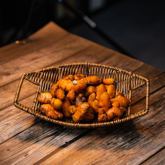 Basket of yellow gingers on wooden surface. Bright and fresh botanicals with curved shapes and green leaves.