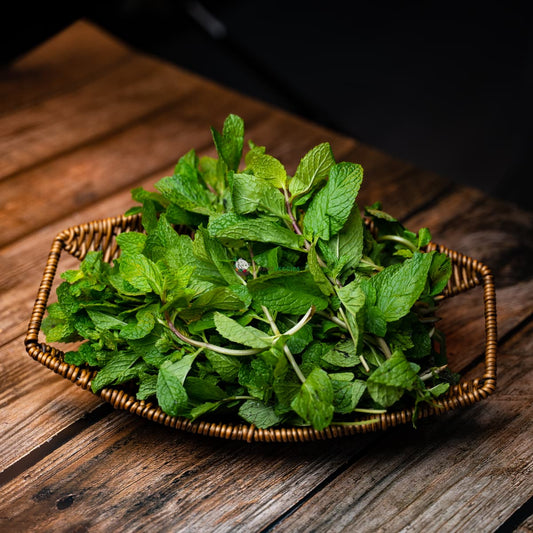 Fresh green mint leaves in a basket on a wooden surface, offering a fragrant aroma and a natural touch.