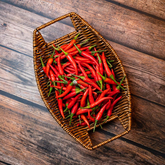 Red chili padi in basket on wooden surface. Spicy small peppers commonly used in Southeast Asian cuisine.