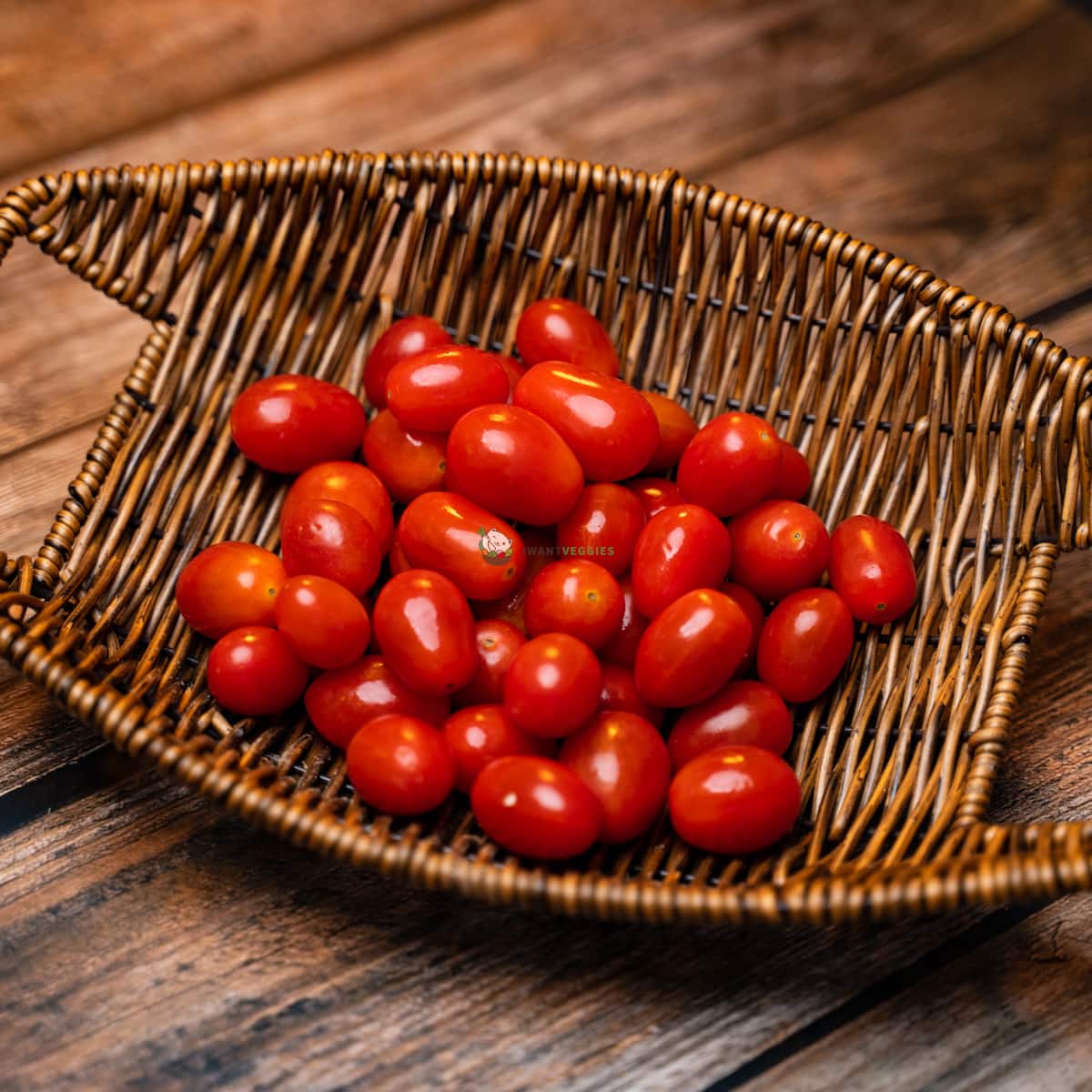 A wooden basket filled with red cherry tomatoes, some of which are still attached to their vines. The tomatoes are ripe and juicy, with a deep red color.