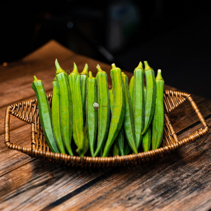 A basket of plump, green lady finger vegetables with a slightly curved shape, sitting on a wooden surface.