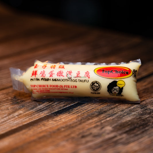 A packet of smooth egg tofu on a wooden basket. Firm, yet silky, with a slightly eggy flavor.