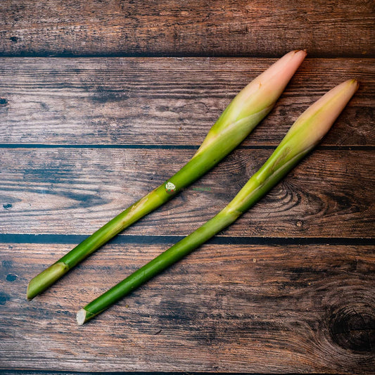 Two ginger flowers on a wooden surface. The flowers are pink and white, with a delicate, feathery texture. They have a sweet, spicy aroma.