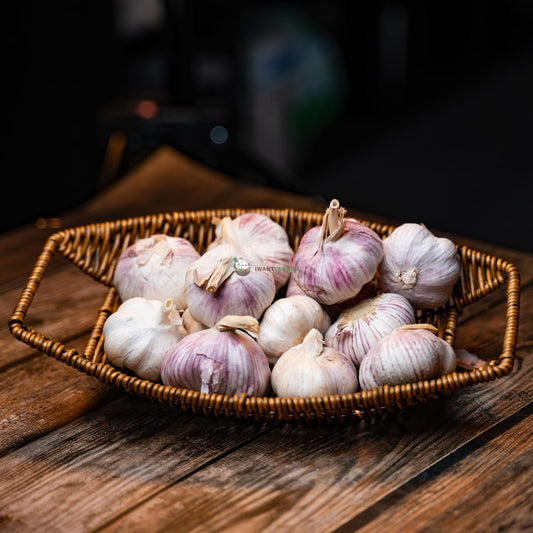 A wooden basket filled with fresh garlic cloves. The cloves are plump and white, with a papery skin. They have a strong, pungent aroma.