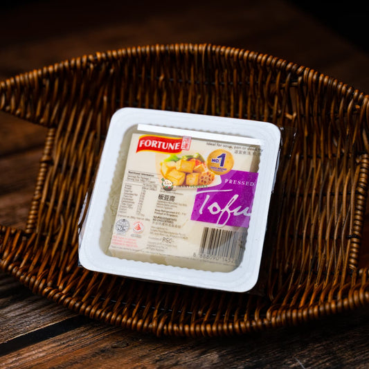 A packet of fortune pressed tofu in a basket on a wooden surface. The tofu is white and firm.