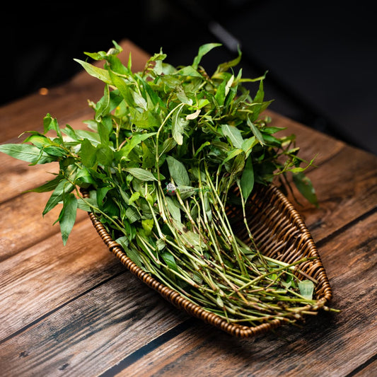 Basket of fresh Laksa leaves on wooden surface, green and aromatic garnish for Southeast Asian cuisine.
