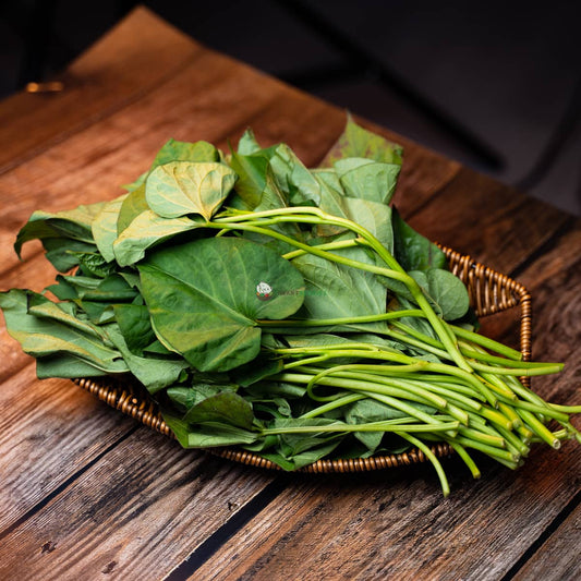Basket of sweet potato leaves on wooden surface; green, vibrant, and fresh.