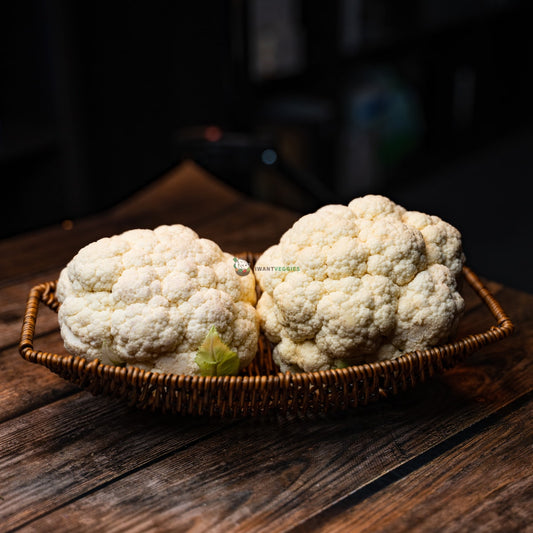 Two fresh Taiwan cauliflowers on a rustic wooden basket. Green leaves with tightly packed white florets.