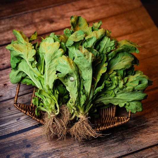 tong ho leaves laid on a basket, on a rustic wooden surface. The leaves are green, smooth, and slightly curled at the edges.